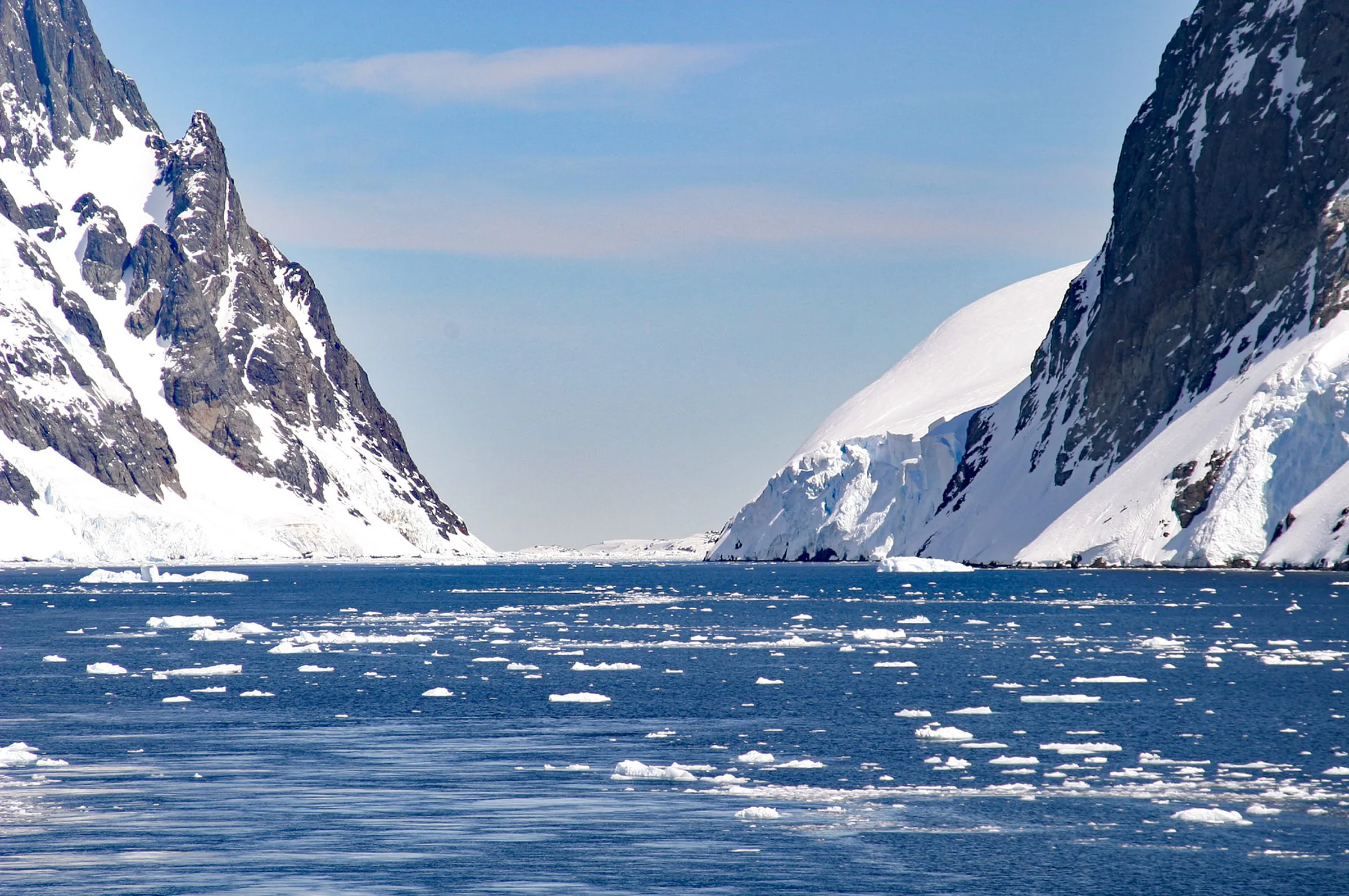 Steep snow and rock walls frame the narrow Lemaire Channel, with scattered brash ice on deep blue water.