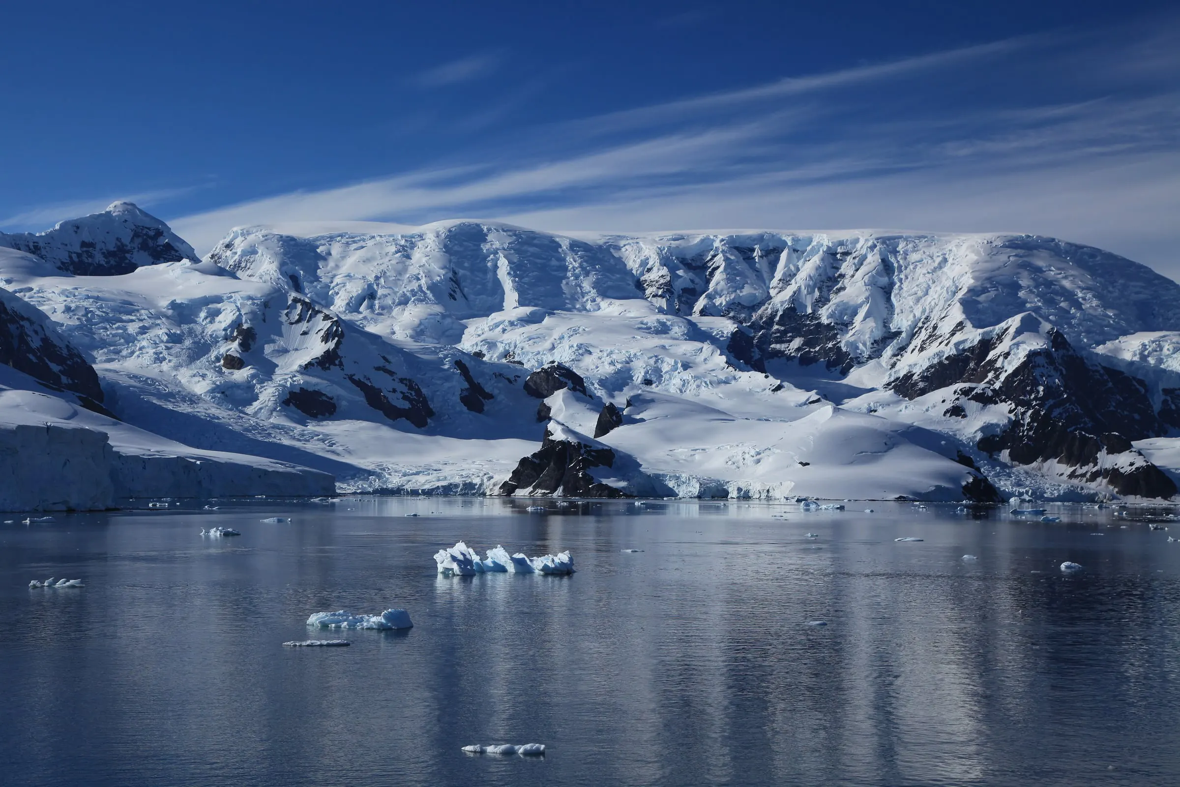 Glaciated mountains rise above the mirror-calm water of Paradise Harbour, with small ice floes in the foreground.