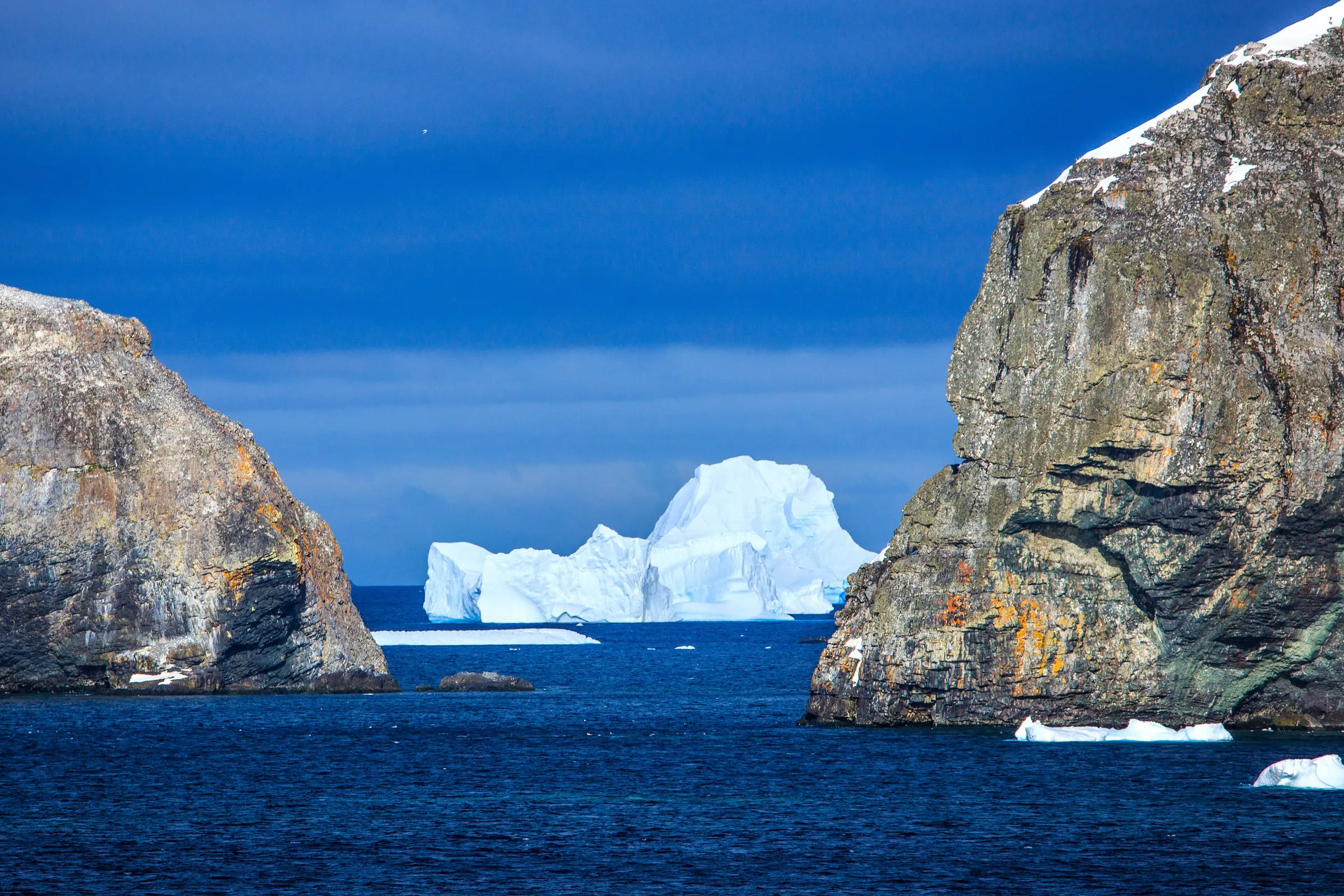 A blue-white iceberg floats between two rocky headlands on the approach to Mikkelsen Harbour, Trinity Island.